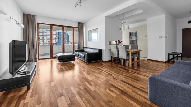 A modern living room with a flat-screen TV, a sofa, a dining area with a table and chairs, and a kitchen in the background. - Bukowińska 22A Apartment with Terrace (Warszawa)