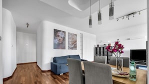 A modern living room with a blue sofa, grey chairs, a wooden dining table, and a TV. - Bukowińska 22A Apartment with Terrace (Warszawa)