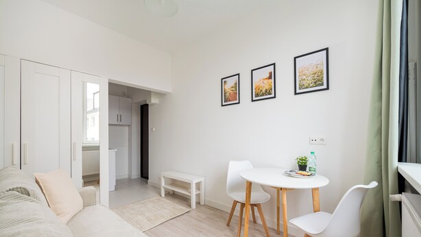 En moderne stue med sofa, spisebord med stole og en lille bænk. Vægmalerier og et vindue med gardiner.