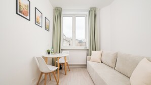 Et lille, lyst rum med en hvid sofa, et rundt bord med to stole og tre billeder i rammer på væggen.