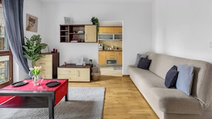 Un salon moderne avec un canapé, une table à manger dressée pour deux personnes, une cuisine en arrière-plan et une grande fenêtre avec des rideaux.