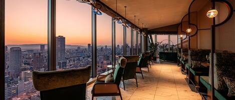 A high-rise interior with a city view, modern furniture, and a bar area.