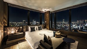 Una habitación de hotel moderna con una cama grande, zona de estar y vistas a la ciudad.