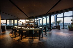 A modern bar area with a circular seating arrangement, large windows, and a city view. - THE GATE HOTEL OSAKA by HULIC (Osaka)