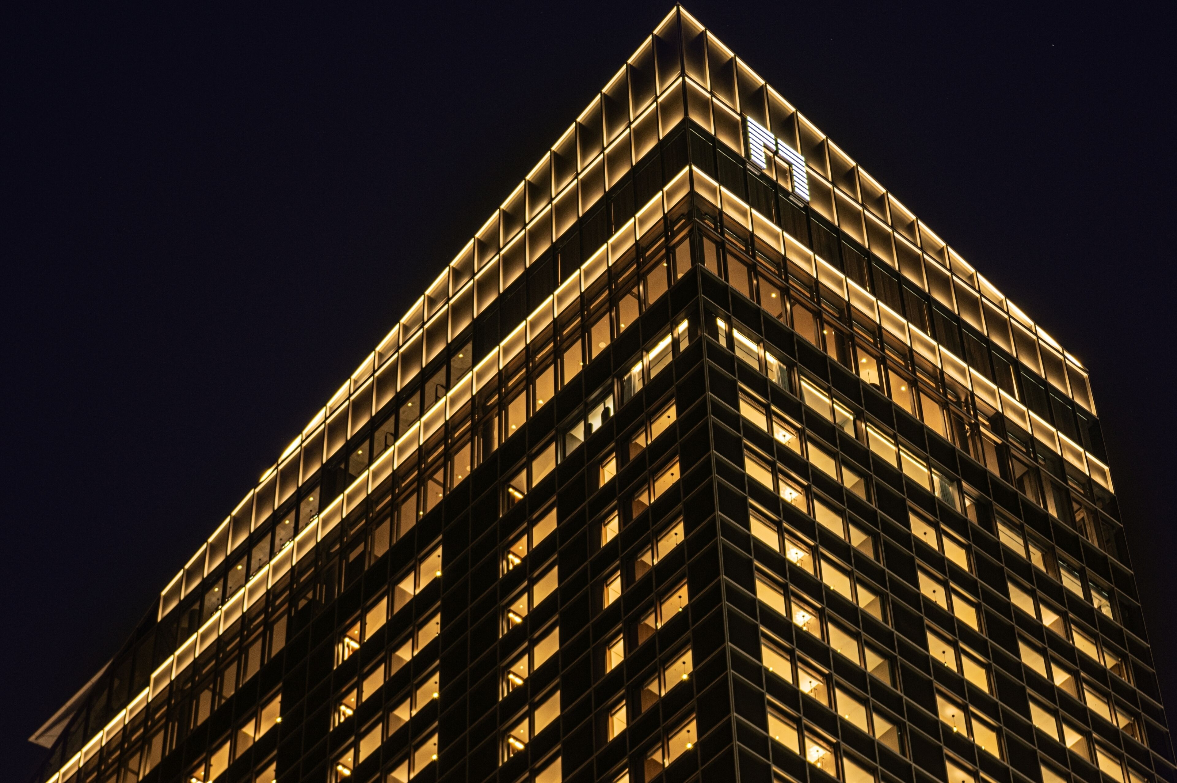 A high-rise building with a grid of windows and a corner illuminated by a lighted sign.