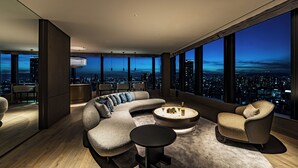 Una sala de estar moderna con un sofá curvo modular, una mesa de centro redonda y vistas de la ciudad a través de amplios ventanales.