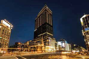 Un edificio alto con un design architettonico moderno, caratterizzato da una struttura angolare di rilievo e numerose finestre illuminate.