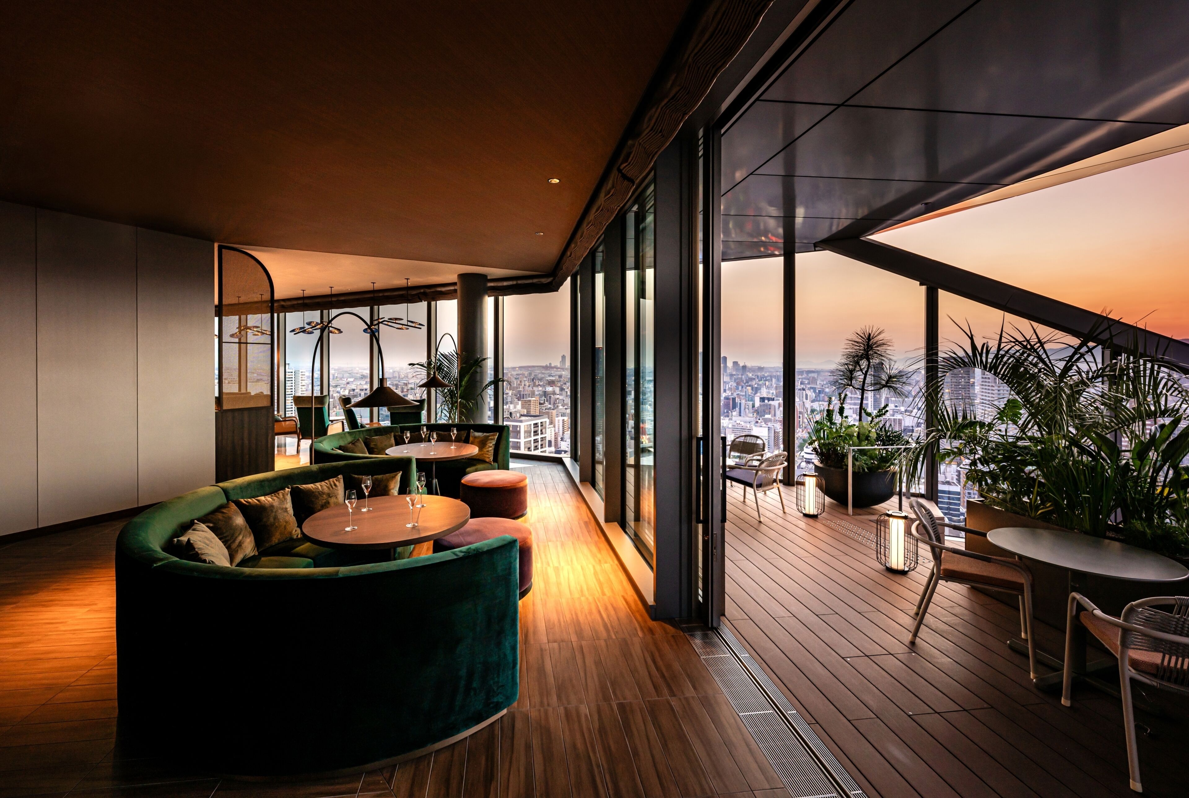 A modern interior with a curved green sofa, round tables, and a city view through large windows.