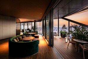 A modern interior with a curved green sofa, round tables, and a city view through large windows. - THE GATE HOTEL OSAKA by HULIC (Osaka)