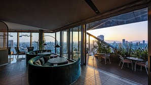 Un interior moderno con una zona de estar curvilínea, una mesa de comedor y vistas de la ciudad a través de amplios ventanales.