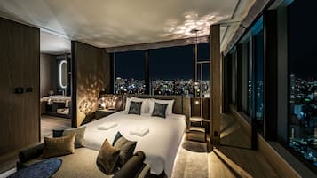 A modern bedroom with a large bed, a sitting area, and a city view.