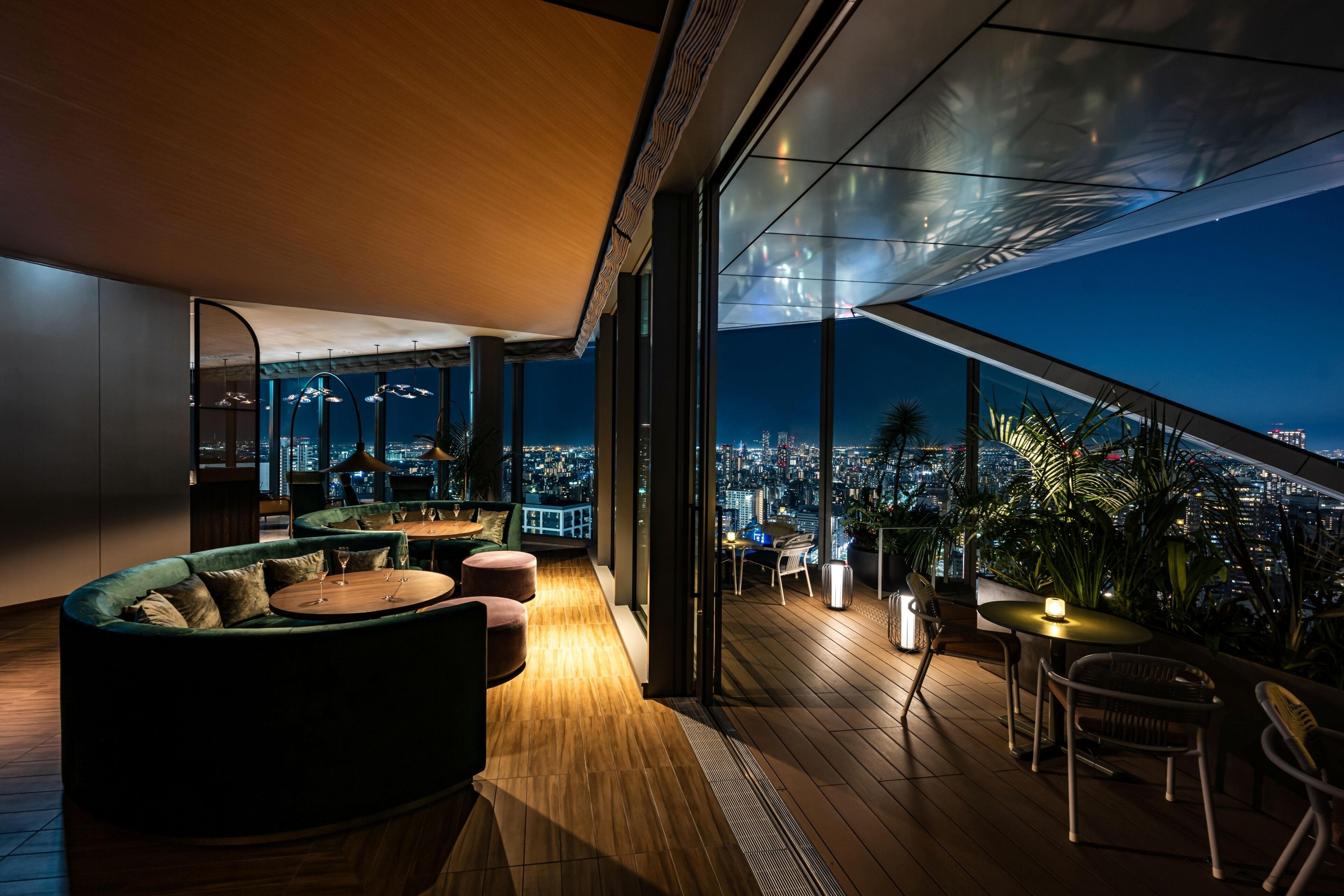 Un salon moderne situé sur le toit, offrant une vue panoramique sur la ville, aménagé avec des canapés et des tables, et doté d’une terrasse en bois.