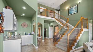 A spacious kitchen with a double staircase, a dining area, and a living room with a couch. - Peckham Point 5 Bd Lake View Retreat w Private Pool (Point Venture)