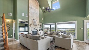 A spacious living room with a fireplace, large windows, and a view of the outdoors. - Peckham Point 5 Bd Lake View Retreat w Private Pool (Point Venture)