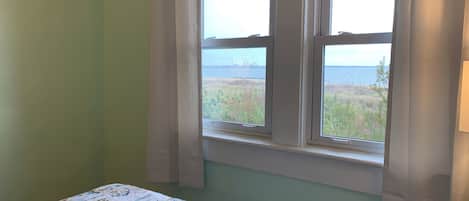 A room with a bed, a window with curtains, and a view of a body of water and a bridge.