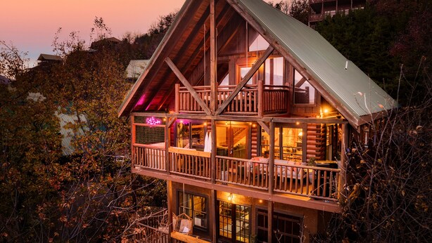 A multi-story log cabin with balconies and large windows, surrounded by trees.