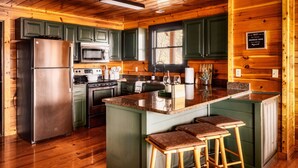 A modern kitchen with green cabinets, stainless steel appliances, and a central island with bar stools.