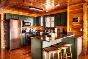 A modern kitchen with green cabinets, stainless steel appliances, and a central island with bar stools.