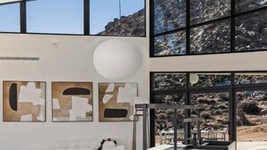 Un interior modern amb zona de menjador, grans finestres i obra d'art abstracta a la paret.