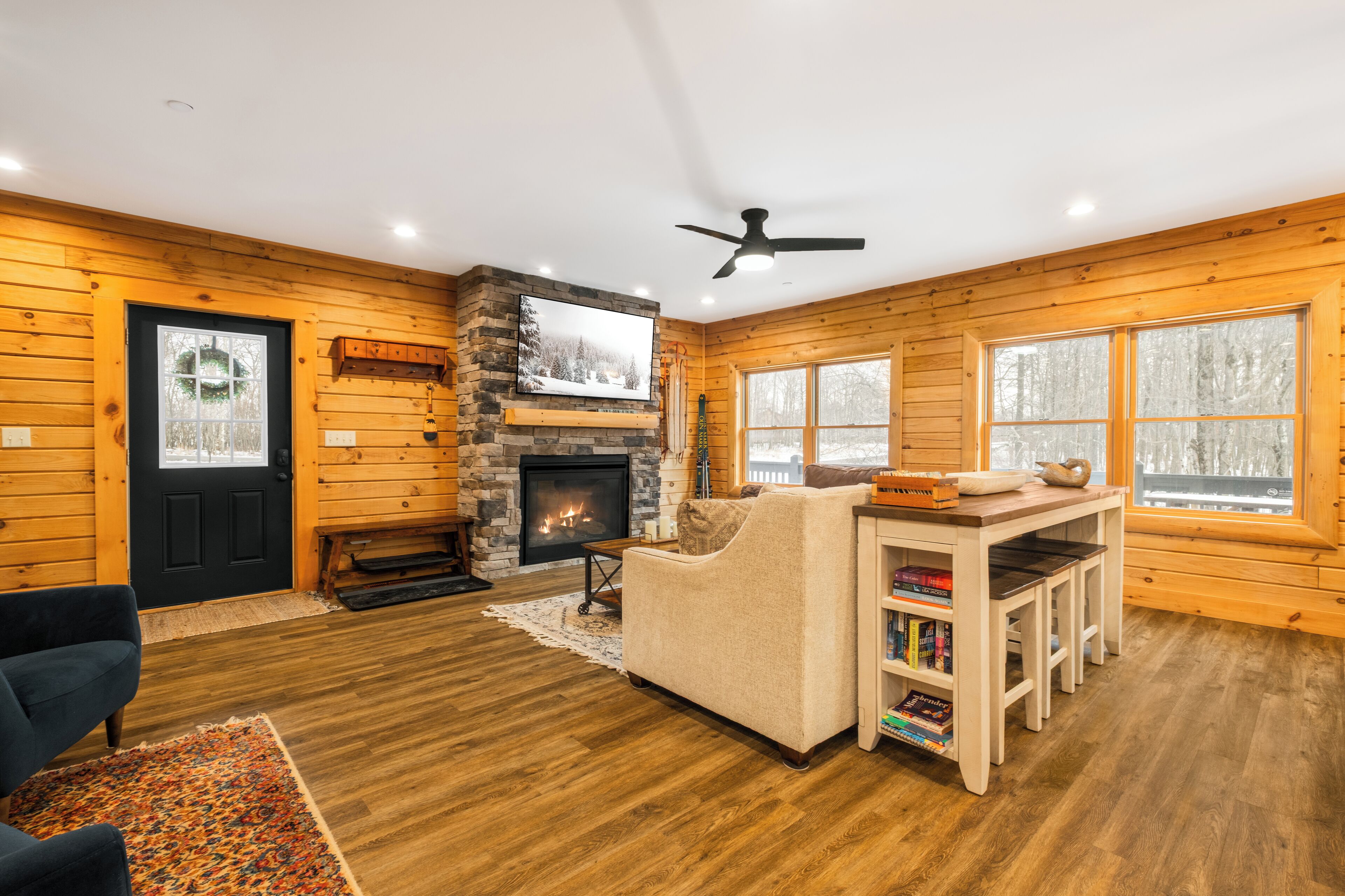 A cozy log cabin interior with a fireplace, a ceiling fan, and a bookshelf.
