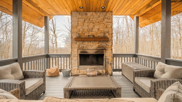A covered outdoor seating area with wicker furniture and a stone fireplace. - Sundance Summit: A 4 BR retreat in a Ski-in/Ski-out Community near Wisp (McHenry)