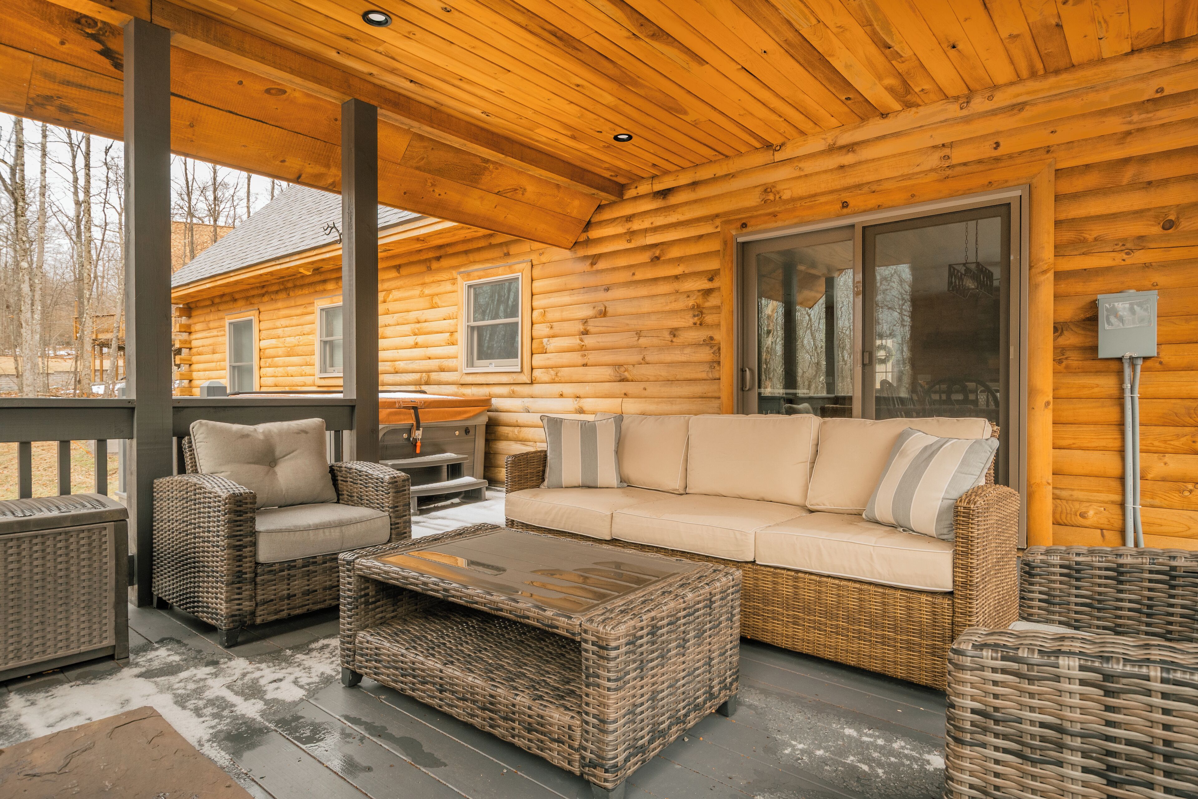 A log cabin with a covered porch, wicker furniture, and a large window.