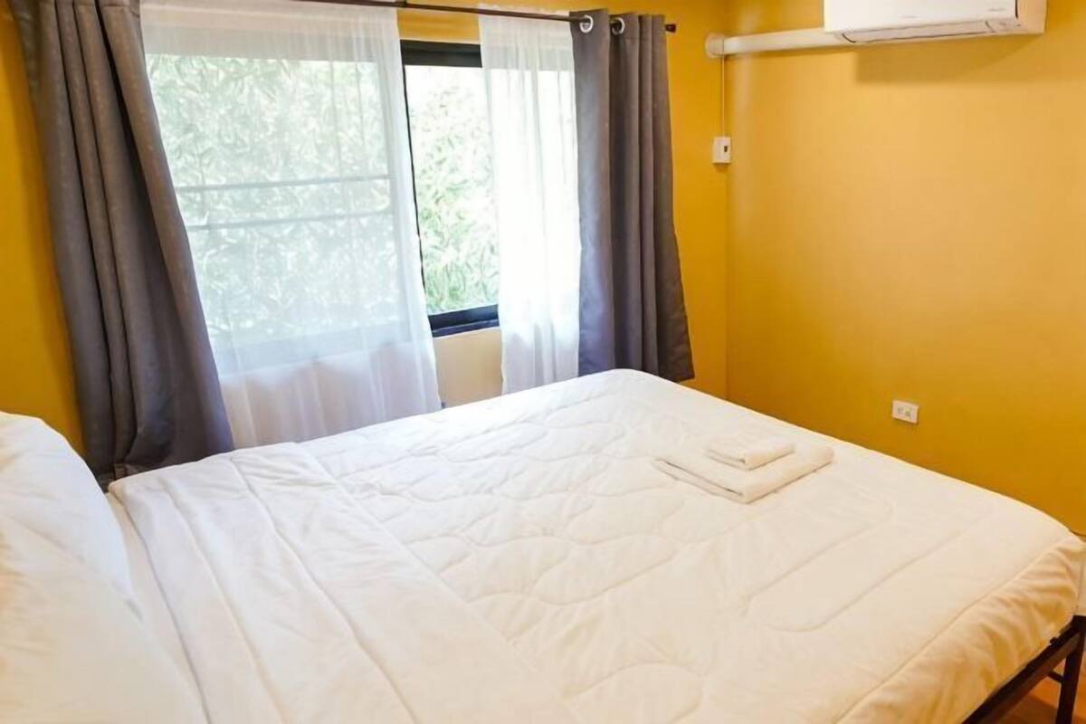 Een kamer met een bed, een raam met gordijnen en een airconditioning aan de muur.