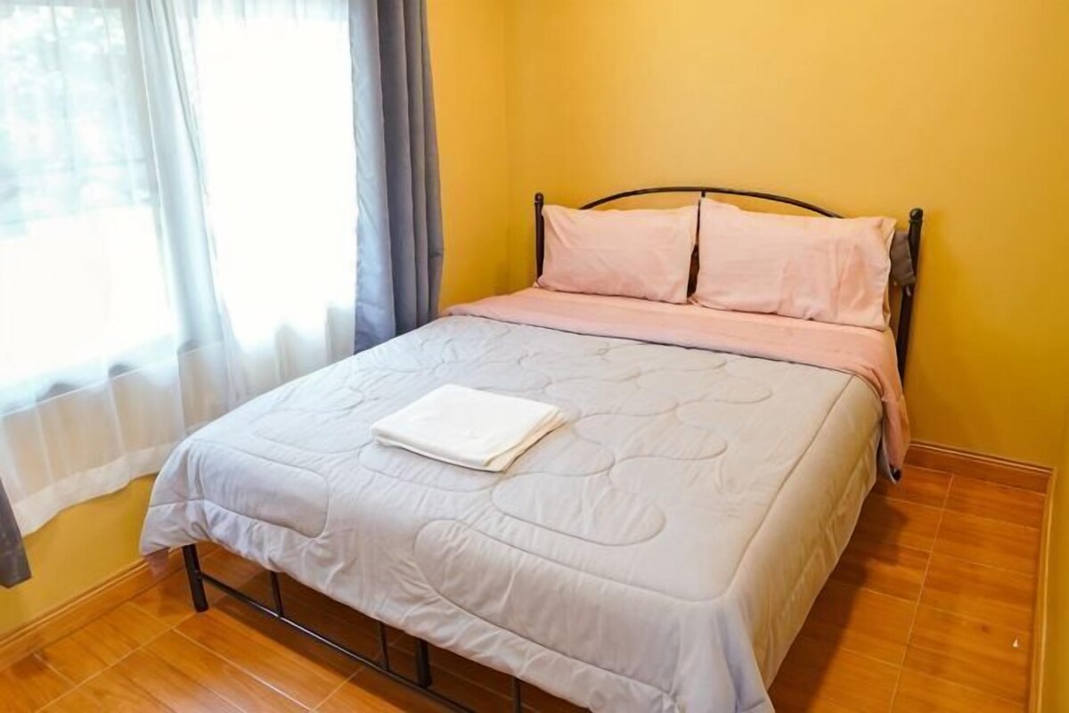 A bed with a white quilt, a wooden floor, and a window with curtains.