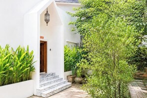 Un bâtiment blanc avec une porte en bois, des marches menant à une entrée abritée et des plantes en pot.