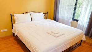 Un lit bien fait, avec du linge de lit blanc et une serviette pliée, une fenêtre avec des rideaux et un plancher en bois.