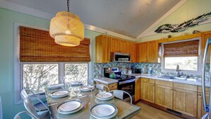 A modern kitchen with wooden cabinets, a microwave, and a dining area with a glass table set for six. - Sound Rider-Canal Front - 4 Minute Drive to Beach and Ramp 49! (Frisco)