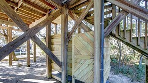 A wooden staircase leading up to a covered area with a large door, surrounded by a wooden deck and trees. - Sound Rider-Canal Front - 4 Minute Drive to Beach and Ramp 49! (Frisco)