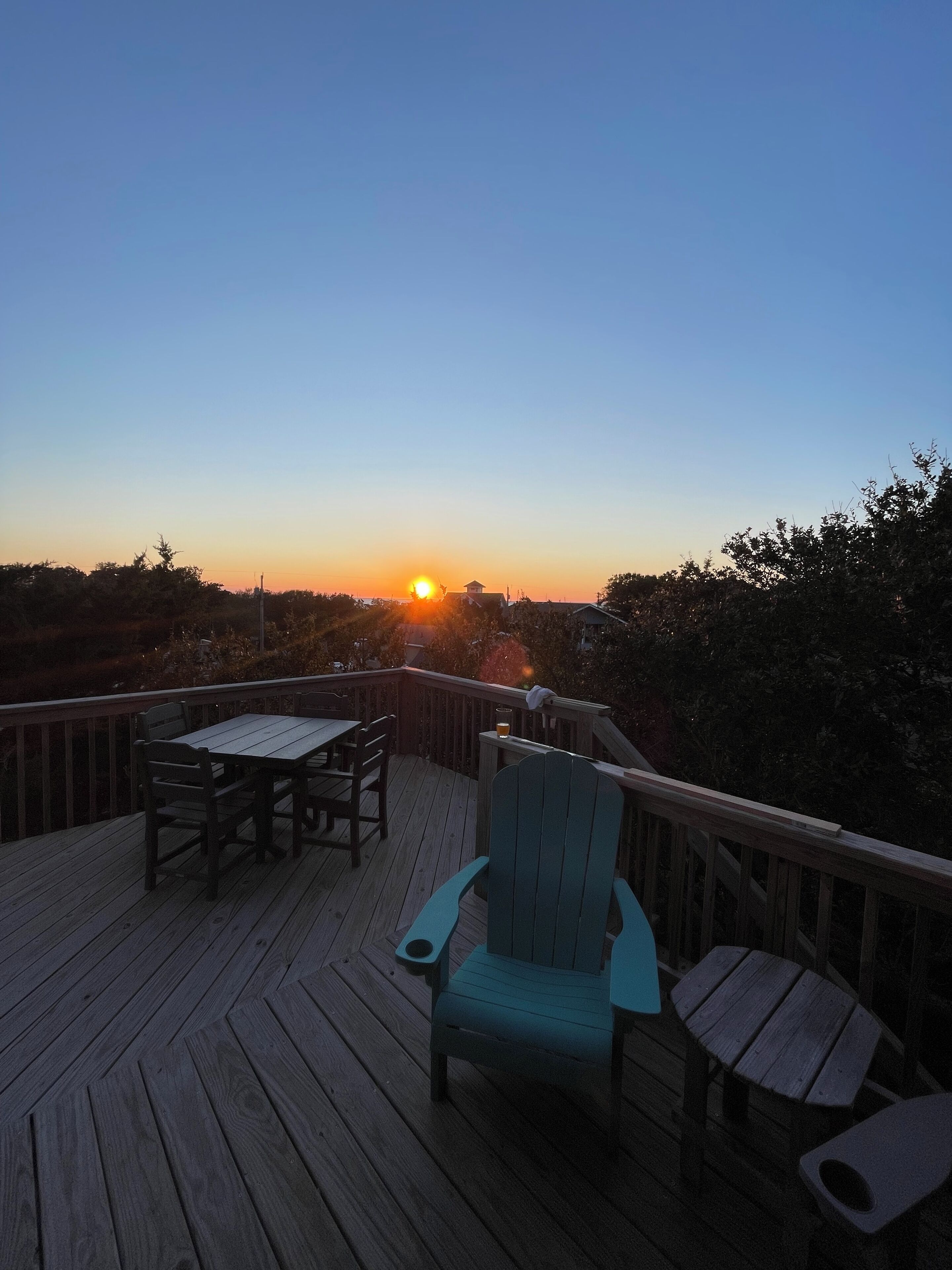 Terraza de madera con mesa y sillas, con vista a un atardecer.