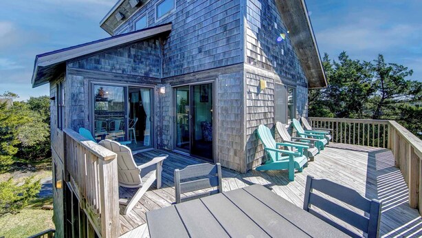 A modern wooden house with a deck, outdoor seating, and large windows. - Sound Rider-Canal Front - 4 Minute Drive to Beach and Ramp 49! (Frisco)
