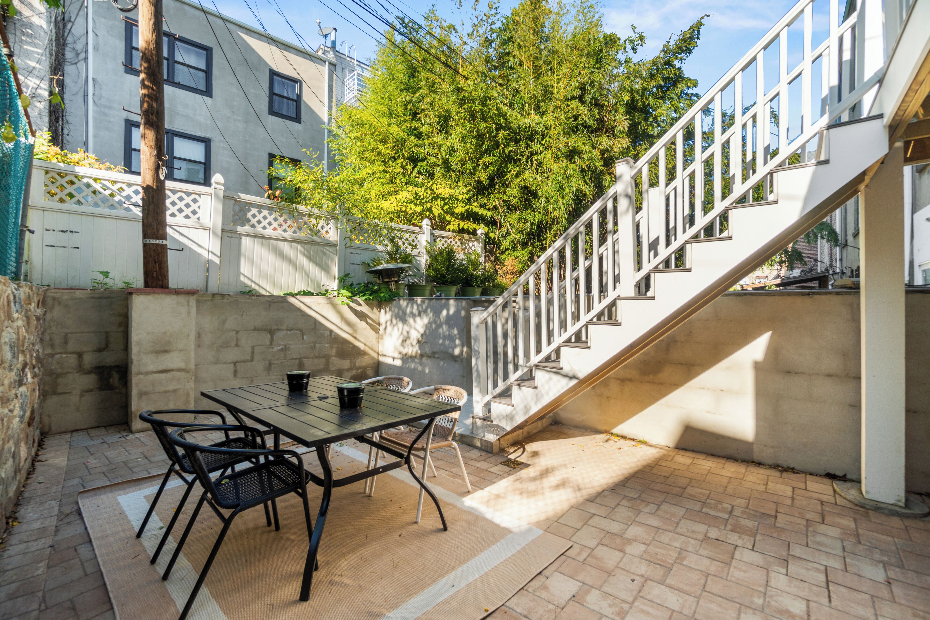 Un patio con una mesa y sillas, un muro de concreto y una escalera que lleva a un nivel superior.