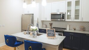 A modern kitchen with a central island, bar stools, a microwave, and a sign indicating WiFi access. - The Blue Pearl Retreat (Houston)