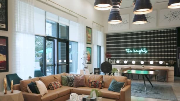 A modern living room with a large sofa, a coffee table, and a small ottoman. There are multiple hanging lights and a green neon sign on the wall. - The Blue Pearl Retreat (Houston)
