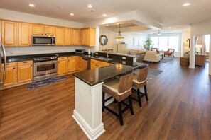A spacious kitchen with wooden cabinets, stainless steel appliances, and a central island with bar stools. - Sandbridge Dunes Condo #218- Pool, Elevator (Virginia Beach)