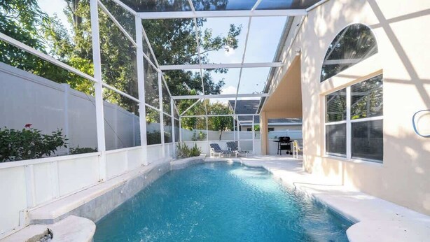 Piscina con cerramiento de vidrio, sillones de descanso y zona de terraza.