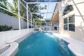 A swimming pool with a glass enclosure, lounge chairs, and a patio area.