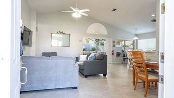 Ein modernes Wohnzimmer mit einer Couch, einem Esstisch mit Stühlen und einem Deckenventilator.