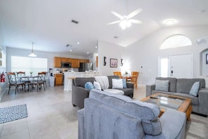 A spacious living area with a grey sofa, a coffee table, and a dining table with chairs.