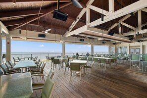 Une terrasse ouverte, avec des tables et des chaises, donnant sur la mer.