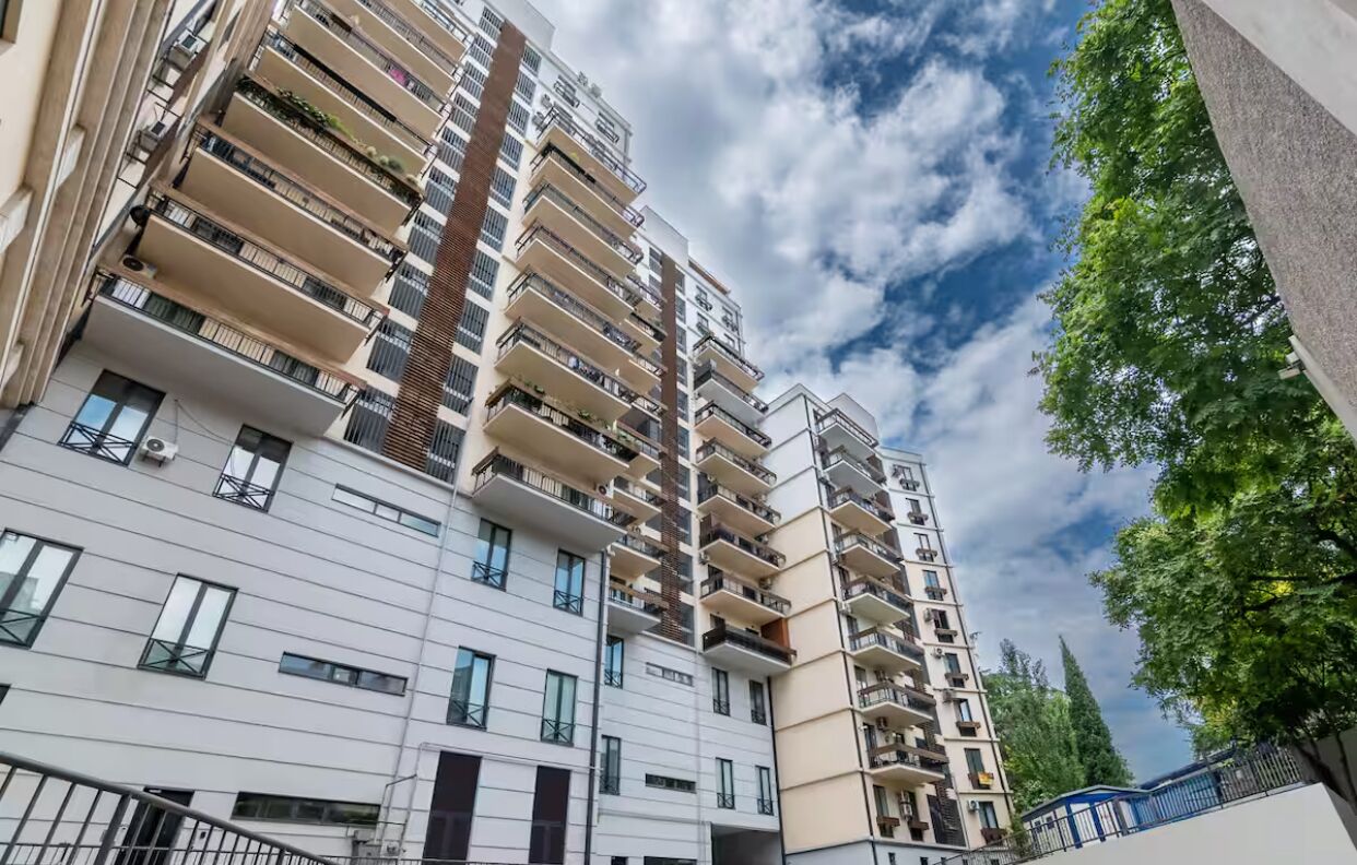 A multi-story residential building with balconies, large windows, and a clear sky.
