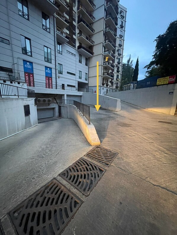 Un immeuble à plusieurs étages doté de balcons, d’une entrée sécurisée par un portail et d’une grille d’évacuation au niveau du sol.