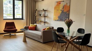 Ein modernes Wohnzimmer mit einer Couch, einem Esstisch mit Stühlen, einem roten Sessel, einer Glasvase mit Blumen und einem großen abstrakten Gemälde an der Wand.
