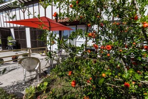 Eine Terrasse mit rotem Sonnenschirm, Gartenmöbeln und einem Garten mit orangefarbenen Blüten.