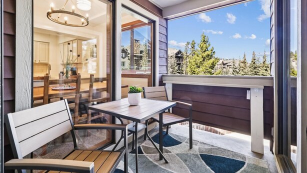 Un balcón con una mesa y sillas, una planta en maceta y vistas a una zona residencial con árboles y casas.