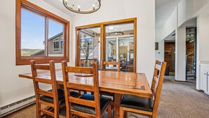 Un comedor con una mesa y sillas de madera, ventanas amplias y un espejo que refleja el interior.