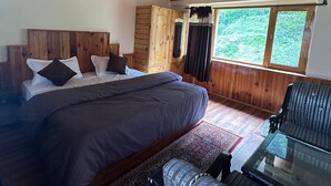 A wooden cabin bedroom with a bed, a sofa, a glass table, and a view of the outdoors. - Hotel Sno Cottage (Manali)